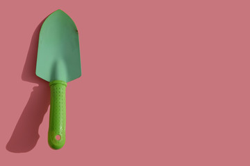 Green spoon shoveling isolated on pink background with copy space for text. Garden tool.