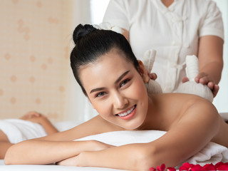 Obraz na płótnie Canvas Beautiful young asian woman lying relaxing and smile on the bed having a massage with herbal compresses in a spa. Thai massage for health. Select focus face women