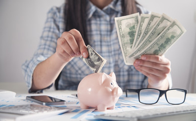 Business girl putting dollar banknote to piggy bank.