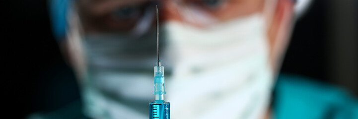 Physician injector arms in sterile uniform holding syringe while operating patient in surgical theatre closeup. HIV protection aids medication botulinum toxin innovation 911 team concept