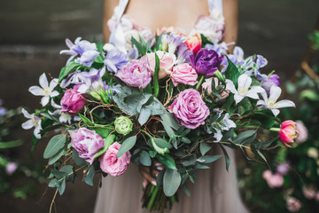 Bride holding b beautiful colorful wedding bouquet of roses, peonies and tulips in bright pink, coral and purple colors.