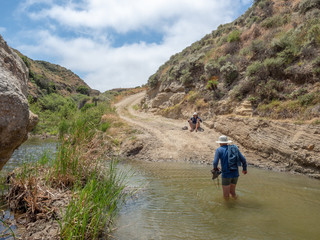 Hikers fording river, Water Canyon Beach, Coastal Road, near Ranch at Bechers Bay Pier on a sunny spring day, Santa Rosa Island, Channel Islands National Park, Ventura, California, USA