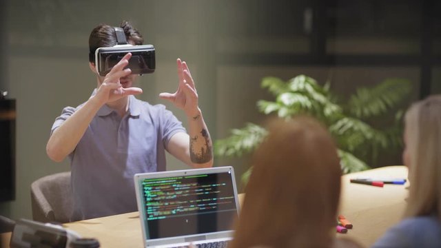 Camera tilting down to man exploring virtual reality during VR software testing near female programmers in modern office