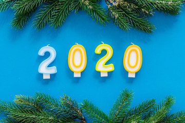 2020 New Year design. Date laid out by candles near fir branches on blue background top view