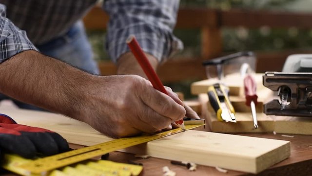 Craftsman adult carpenter with a pencil and the carpenter&rsquo;s square trace the cutting line on a wooden table. Construction industry, housework do it yourself. Footage.