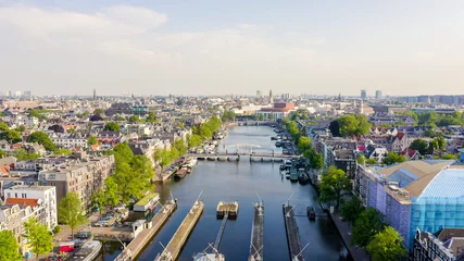 Schilderijen op glas Amsterdam, Netherlands. Flying over the city rooftops. Amstel River, Amstel Gateways, Aerial View © nikitamaykov