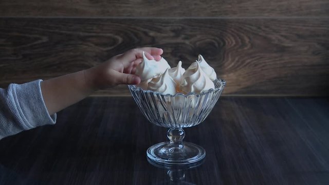 Hand of small kid taking piping meringue cake from glass bowl, close up