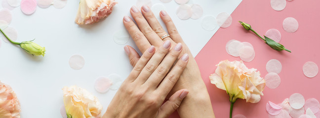 Stylish trendy female pink manicure. Beautiful young woman hands on pink and white background with flowers and place for text. Minimal creative concept. Flat lay, top view, mock up copy space template
