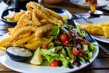 Deep fried salt and pepper calamari with potato chips and vegetable salad on a restaurant table.