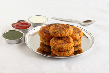 Kabuli chana tikkis, or chickpea patties, a healthy, vegetarian, delicious, and Indian food, with green chutney, ketchup, and curd, stacked on a steel plate.
