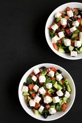 Homemade Shepherds salad with cucumbers, feta and parsley in white bowls on a black surface, top view. From above, overhead, flat lay. Copy space.