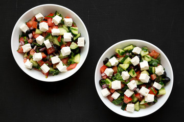 Homemade Shepards salad with cucumbers, feta and parsley in white bowls on a black backgrounds, top view. From above, overhead, flat lay. Close-up.
