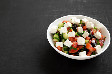 Homemade Shepherd's salad with cucumbers, parsley and feta in a white bowl over black background, side view. Copy space.