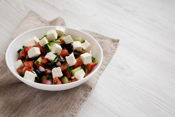 Homemade Shepherds salad with cucumbers, parsley and feta in a white bowl on a white wooden surface, side view. Copy space.