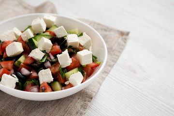 Homemade Shepherds salad with cucumbers, parsley and feta in a white bowl on a white wooden surface, side view. Space for text.