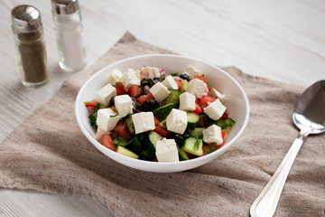 Homemade Shepards salad with cucumbers, parsley and feta in a white bowl on a white wooden background, side view. Closeup.