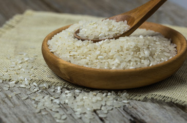 raw white rice (Thai Jasmine rice) in brown bowl and and ear of rice or unmilled rice on wooden background