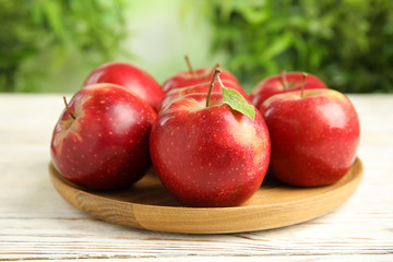 Wooden plate with ripe juicy red apples on white table against blurred background