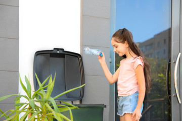 Girl throwing plastic bottle into recycling bin outdoors