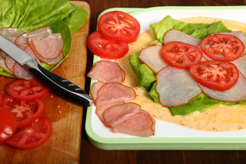 Making wrap tortilla sandwich with ham, tomato, lettuce.