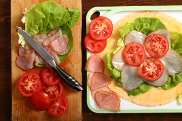 Making wrap tortilla sandwich with ham, tomato, lettuce.