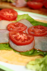 Making wrap tortilla sandwich with ham, tomato, lettuce.