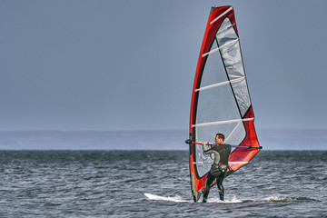 A male athlete is interested in windsurfing. He moves on a Sailboard on a large lake on an autumn...
