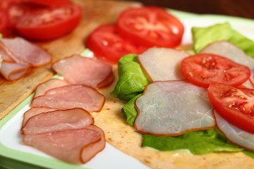 Making wrap tortilla sandwich with ham, tomato, lettuce.