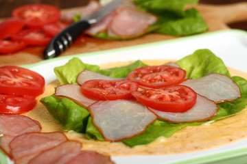Making wrap tortilla sandwich with ham, tomato, lettuce.