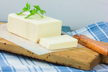 A few slices of yellow butter cut off from a just opened pack of butter with a knife on a brown wooden cutting board.