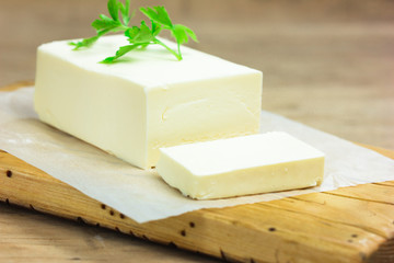 A few slices of yellow butter cut off from a just opened pack of butter with a knife on a brown wooden cutting board.