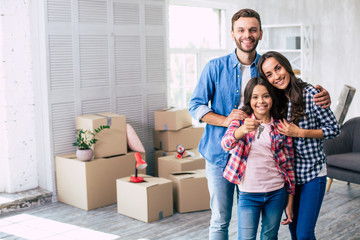 Fototapeta na wymiar The new page of our story. Delightful parents are hugging their teenage daughter who is holding a key to their new apartment.