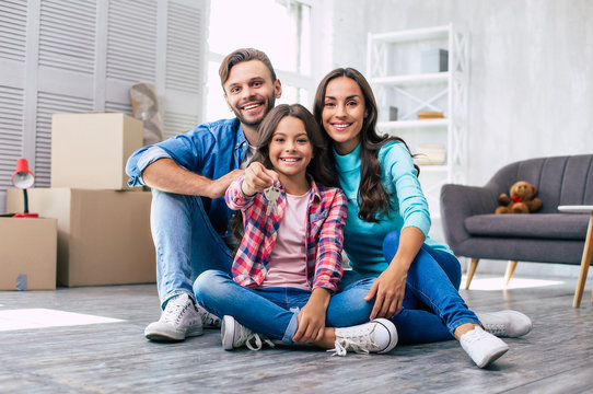 New life starts now. Appealing family are sitting on the floor, holding keys of their new apartment, and enjoying their new life in the new house.