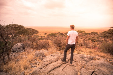 Man at view point looking to the bush savannah of Serengeti at sunset, Tanzania - Safari in Africa