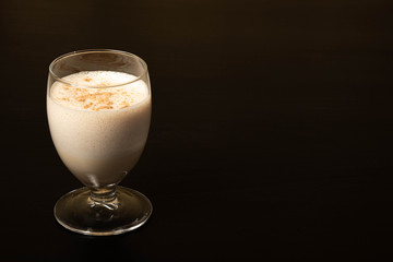 Eggnog Christmas cocktail in a transparent wine glass, sprinkled with grated nutmeg. Isolated on a black background. Copy space.