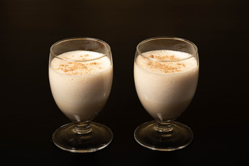 Eggnog Christmas cocktail in a transparent wine glass, sprinkled with grated nutmeg. Isolated on a black background.