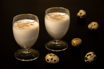 Eggnog Christmas cocktail in a transparent glass, sprinkled with grated nutmeg, on a black background with quail eggs.