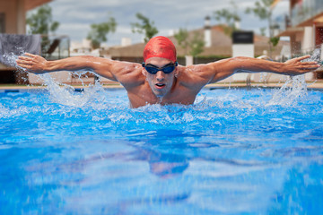 Swimmer in an outdoor pool, swimming butterfly-style, with open arms and with a speedy face