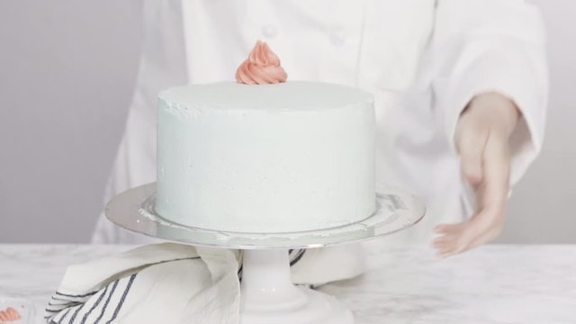 Step by step. Piping buttercream rosettes on top of round three-layer vanilla cake.