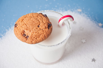 Glass of milk, cookies and candy cane on the blue background