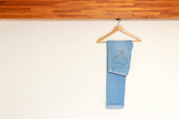 Light blue denim pants hanging on wood hanger on minimal open closet storage with copy space on...