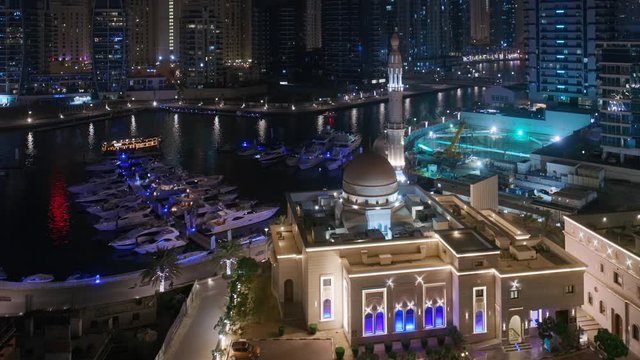 Yachts in Dubai Marina flanked by the Al Rahim Mosque with parking and residential towers and skyscrapers aerial night view. Modern high rise skyline with boats and wooden dhows