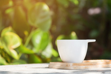 Coffee cup on wooden table in garden with bright green background; copy space 