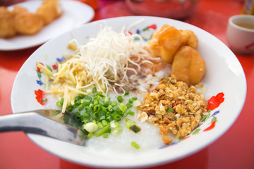 Pork rice porridge with soft-boiled egg, deep-fried dough stick, sliced ginger, spring onion and fried garlic served with hot chinese tea at local morning market.