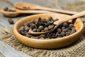 Black peppercorns in a small white bowl over stone background.