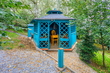 Lovely turquoise gazebo in garden. Resting place with trees and shrubs in the background. Garden architecture concept.