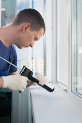 master in protective gloves, seals the cracks of the plastic window with white silicone