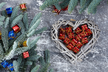 Christmas composition. red and blue gift boxes in a wicker basket in the shape of a heart, fir branches on a gray background, Flatlay