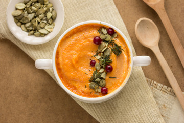 Pumpkin soup and organic pumpkins on rustic wooden table. Seasonal autumn food - Spicy pumpkin soup with thyme and pumpkin seeds.