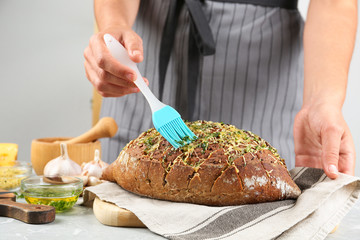 Woman brushing tasty homemade bread with garlic and herbs at light table, closeup